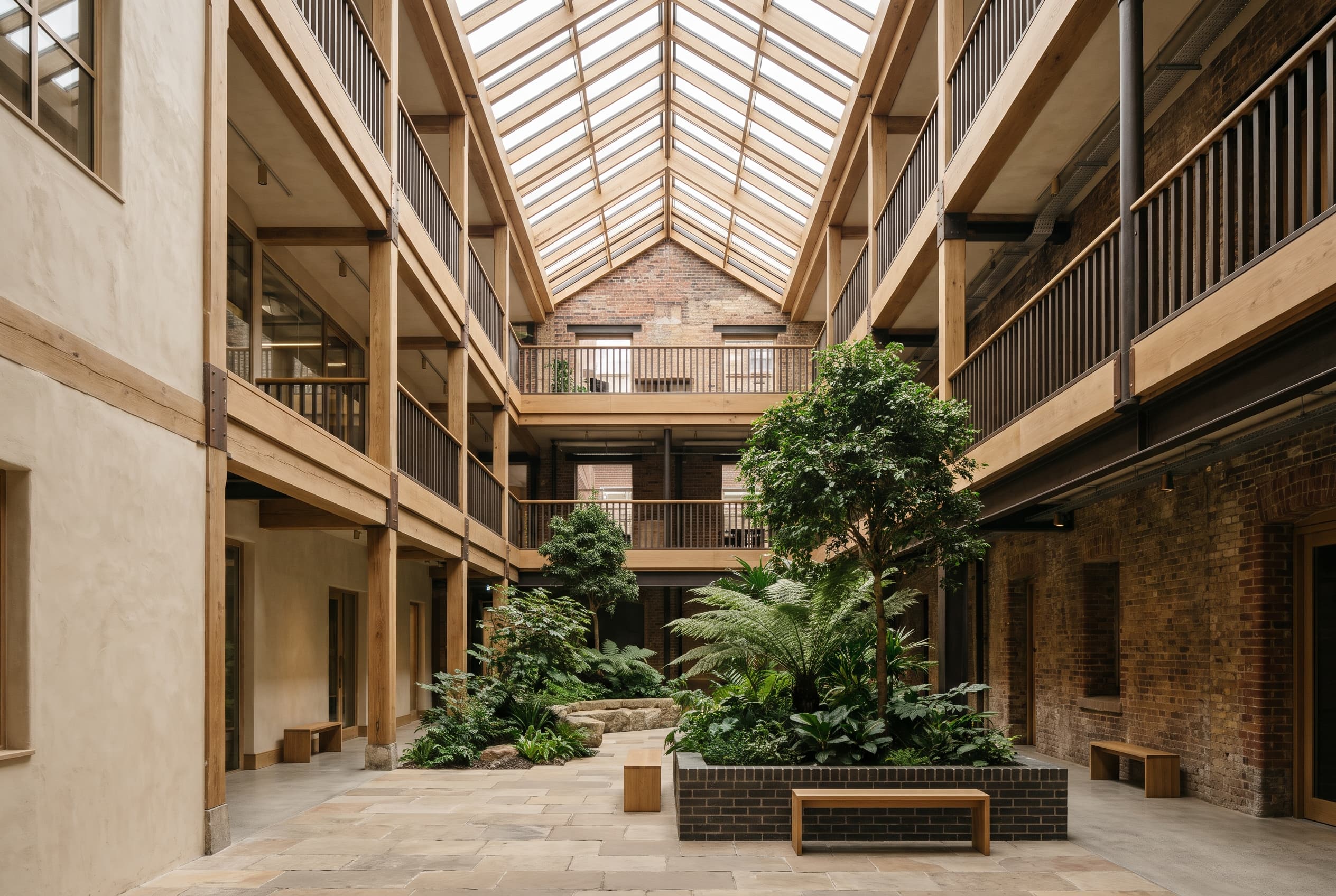 Planted atrium with mature trees and timber galleries inside a brick warehouse under a long rooflight